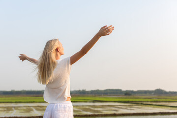 Fototapeta na wymiar Happy blonde woman feeling at peace standing in a rice field with arms open towards the blue sky in Vietnam. 