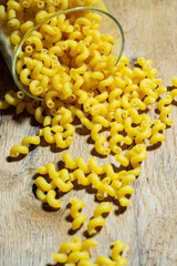 Uncooked golden wheat curly pasta on a wooden background