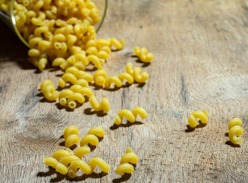 Uncooked golden wheat curly pasta on a wooden background