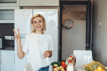 Caucasian blonde lady gesturing the peace sign while unpacking products bought during the lockdown