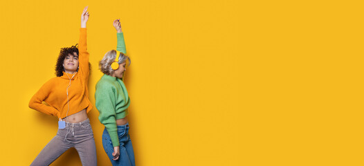 Caucasian women with curly hair listening to music and dance wearing headphones on a yellow wall with free space