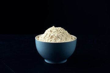 Bowl with wheat flour on the dark blue textured background. Preparation for home backing