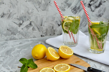The process of making lemonade. On a wooden Board is a Lemon and mint next to a knife. There are glasses of lemonade in the background. Summer drink. Lemonade with lemon and mint. Selective focus
