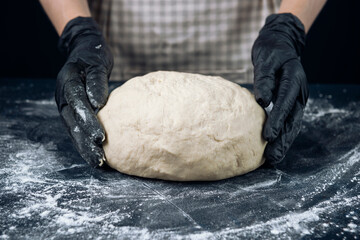 Woman in checkered apron and black gloves prepare a piece of yeast dough. Process of making bakery. Adjarian Khachapuri Recipe – Georgian cheese bread.