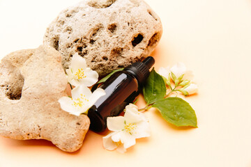 Beautiful composition with tea oil. Glass cosmetic bottles stand on a stone with jasmine on a beige background with bright sunlight. Natural cosmetics concept, natural essential oil.