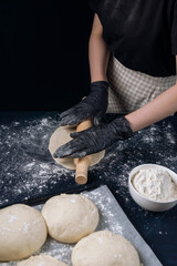 Woman in black gloves rolling out yeast dough with a rolling pin. Process of making bakery. Adjarian Khachapuri Recipe – Georgian cheese bread.