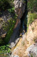 Unrecognizable person canyoning with ropes under the stream