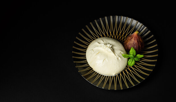 Traditional Italian, fresh, soft white burrata cheese, mozzarella ball with cream, Fig fruit on a round dark plate, on a dark background. copy space.