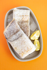 frozen raw cod fish with ice on dish on orange background