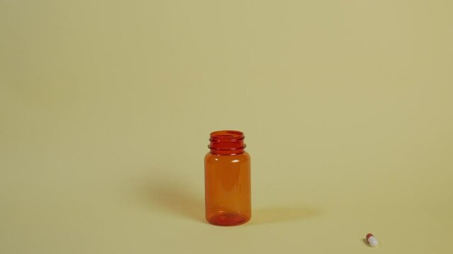 Slow motion wide shot of a pill as it falls vertically towards an open pill bottle and bounces off the rim.