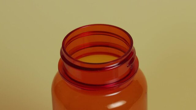 Slow motion high-angle close-up of a pill bottle as pills fall, eventually filling the bottle.