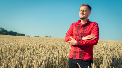 Naklejka na ściany i meble Portrait of a young handsome man in Ukrainian folk traditional costume, red in a golden wheat field.