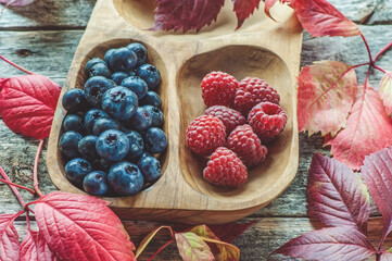 wild berries, lots of blueberries and raspberries in an eco-friendly wooden Cup on a wooden table with autumn leaves