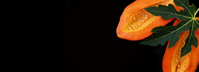 Mock-up banner fresh and tasty papaya cut in half with papaya leaf on a black texture background....