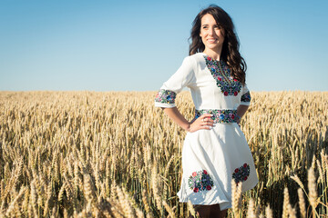 A young, pretty, pretty girl in a Ukrainian folk traditional shiny costume in a golden wheat field.