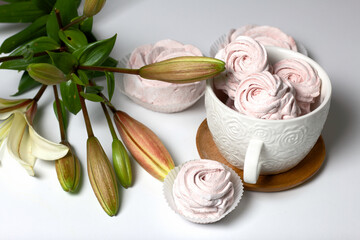 Homemade zephyr of various shapes. In a mug and on the surface of the table. Near a lily with unblown buds.
