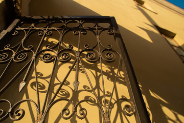 Iron forged grate fence gate contrast shadow on the wall in the morning light. Warm yellow brown...