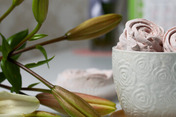 Homemade zephyr of various shapes. In a mug and on the surface of the table. Near a lily with unblown buds.