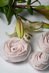 Homemade marshmallows of various shapes. Lies on the surface of the table. Near a lily with unblown buds.