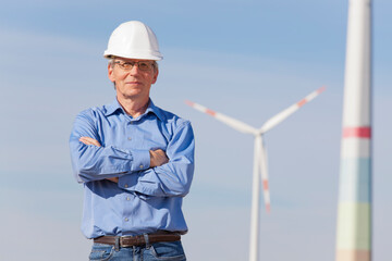 Smiling engineer with hard hat  in front of a windmill