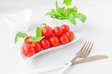 cherry tomatoes and spinach in a beautiful white dish on a light background. To close. Fresh...