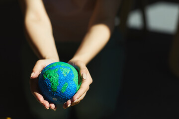 Close-up of unrecognizable woman holding planet model in hands in sunlight, saving Earth concept