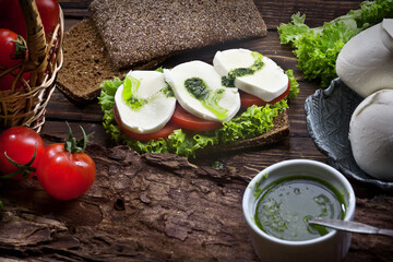 kitchen table with mozzarella sandwich, salad, tomatoes and dark bread, rustic wooden background