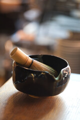matcha green tea praparation kit of black ceramic bowl and bamboo whisk on table, closeup