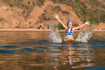 Happy summer. Little girl child jumps out of the water with splashes and drops and with open hands, joy and fun during the summer vacation