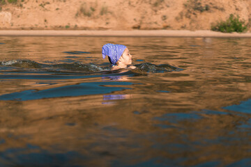 Baby girls swimming in the sea against the background of sandy rocks, one head is visible above the water, learning to swim