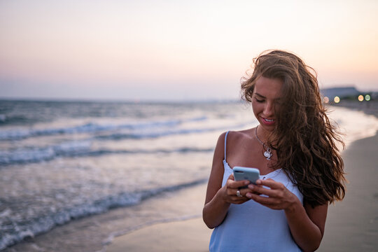 Young smiling woman using smartphone on beach at sunset