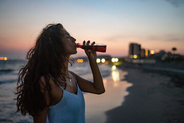 Young woman relaxing at beach and drinking soda at sunset