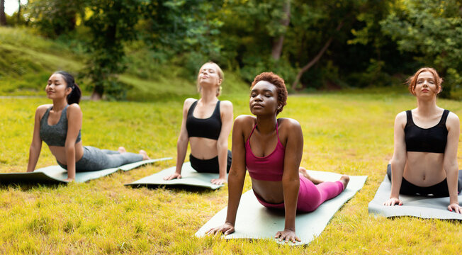 Group of multiracial women attending outdoor yoga class, doing cobra pose together