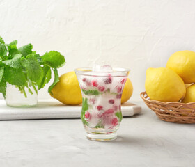 transparent glass with lemonade and pieces of ice, red berries on a white background