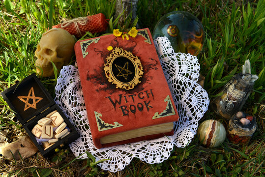 Witch book with decorated cover, runes and skull on the lace in the garden. Esoteric, gothic and occult background with magic objects, mystic and fairy tale concept