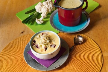 Table with cauliflower soup in bowl and pot, raw vegetable.