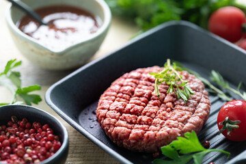 Raw burger cutlets with salt, pepper, herbs and spice for grilling on a wooden table.