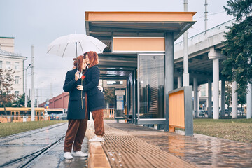 man woman cuddling in the rain. young couple together under an umbrella at a transport stop