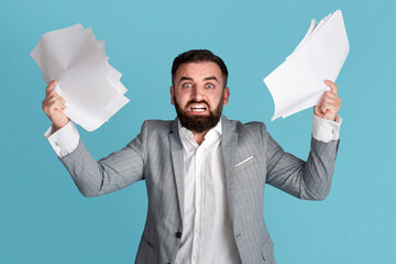 Dealing with workplace stress. Angry overworked office employee grasping paper documents over blue...