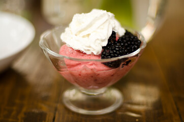 cup with fruit ice cream, blackberries and whipped cream on the table