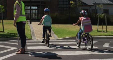 Rear view of two girls with school bags riding bicycles and crossing the road