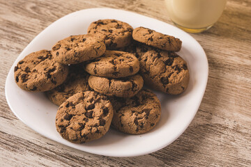 some chocolate cookies on a white plate with a glass of milk