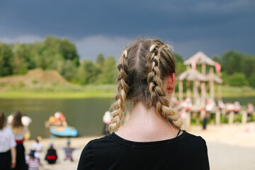 Girl from the back with two braided braids on the bitch with other people (ombre hair, stormy cloudy sky and lake) 