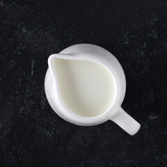 Whit milk jug with milk on a black background, top view.