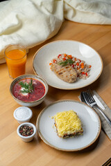 Russian cuisine: coated herring, borscht, pearl barley with fruit drink on wooden cafe table