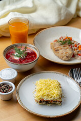 Russian cuisine: coated herring, borscht, pearl barley with fruit drink on wooden cafe table