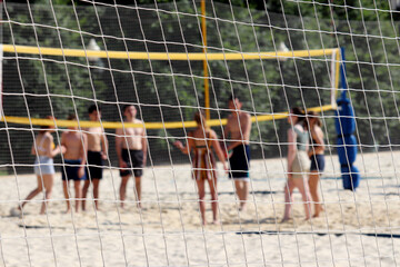 Beach volleyball, summer sport. View through a rope net to people playing ball in the sand, selective focus
