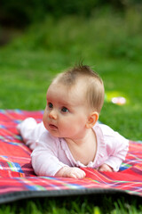 Newborn baby on blanket over green grass. Child having fun on family summer picnic.