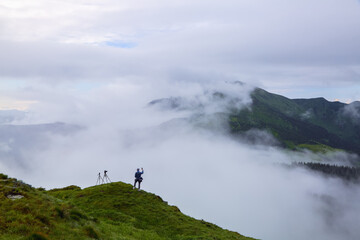 Photographer tourist stays on the hill. Foggy summer morning. Landscape of high mountains and forests. The sun rays are shining through the fog. Wallpaper background. Free space for text.