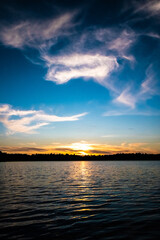 Panorama of a gorgeous sunset at a forest lake, with gold and blue color in the sky and trees reflected in the water. High quality photo